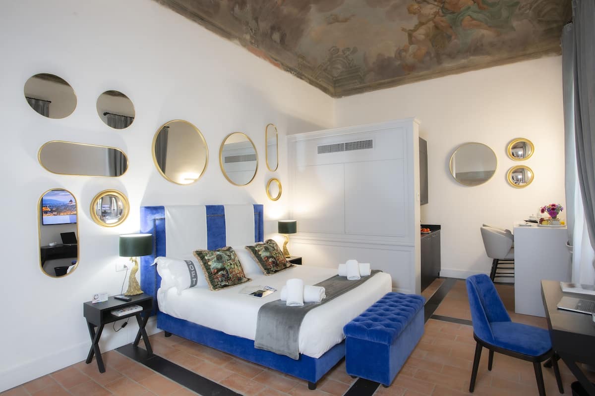 Habitación de hotel con una cama grande, un escritorio, una silla y varios espejos en las paredes.
