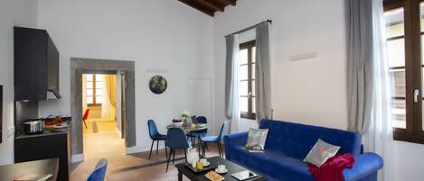 A living room with a blue sofa, a dining table with chairs, and a kitchen area with a stove.