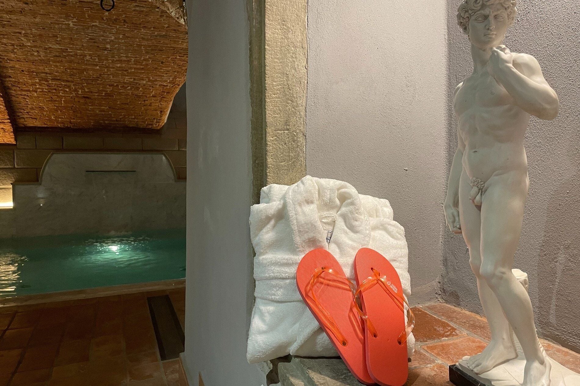 Una statua raffigurante un uomo, una piscina e un paio di ciabatte arancioni su un pavimento piastrellato.