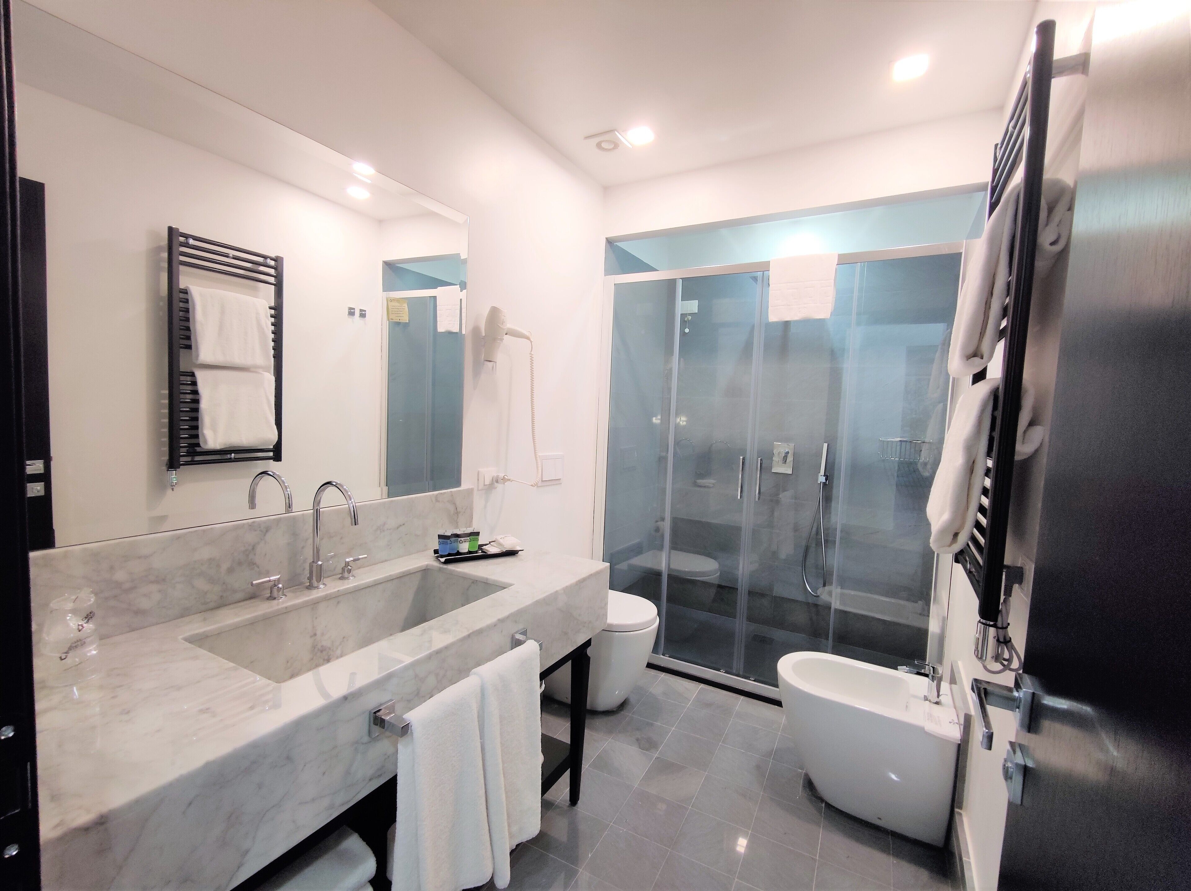 Une salle de bain moderne dotée d’un grand lavabo en marbre, de toilettes séparées, d’une douche à parois de verre et d’un porte-serviettes intégré.