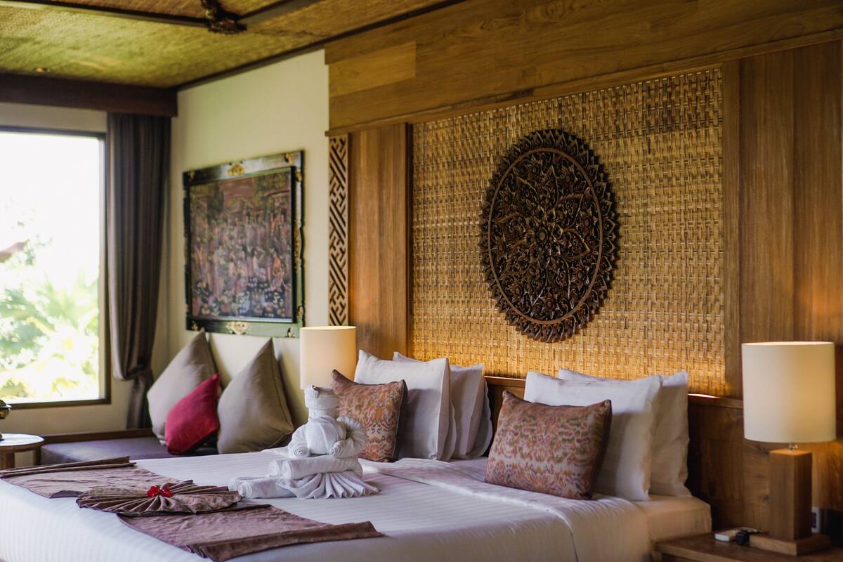 A neatly made bed with pillows and a towel, a decorative wall hanging, and a lamp on a bedside table.
