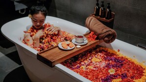 Una vasca da bagno piena di petali colorati, un vassoio con una tazza di tè e degli snack, e un asciugamano.
