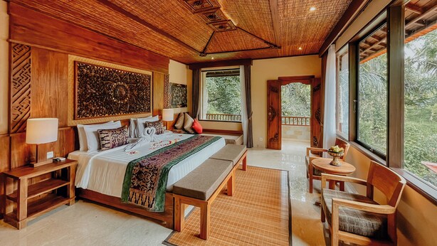 Un'ampia camera da letto con un grande letto, un'area relax con una panca e vista all'esterno tramite ampie finestre.