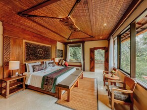 Um quarto espaçoso com uma cama grande, um espaço de estar com um banco e vista para o exterior por grandes janelas.