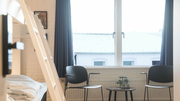 A room with a bed, two chairs, a small table with a plant, and a window with curtains. - Bankbox Hostel Aabybro (Aabybro)
