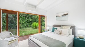 A bedroom with a bed, nightstands, a chair, and a view of a garden through glass doors.