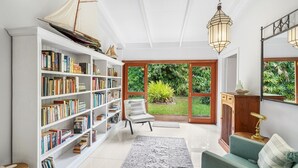A well-lit reading area with a bookshelf, a comfortable chair, and a view of a lush garden through a glass door.