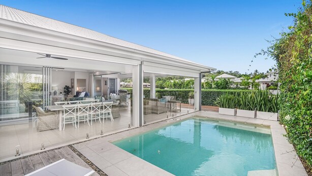 Un espace piscine extérieur moderne, doté d’un patio couvert, de portes vitrées donnant sur un espace de vie et d’un jardin bien entretenu.