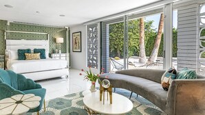 Un dormitorio moderno con una cama grande, una zona de estar con sofá y mesa de centro, y vistas al exterior a través de amplios ventanales.