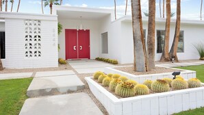 Un edificio moderno con puerta roja, paredes blancas y un jardín de cactus.