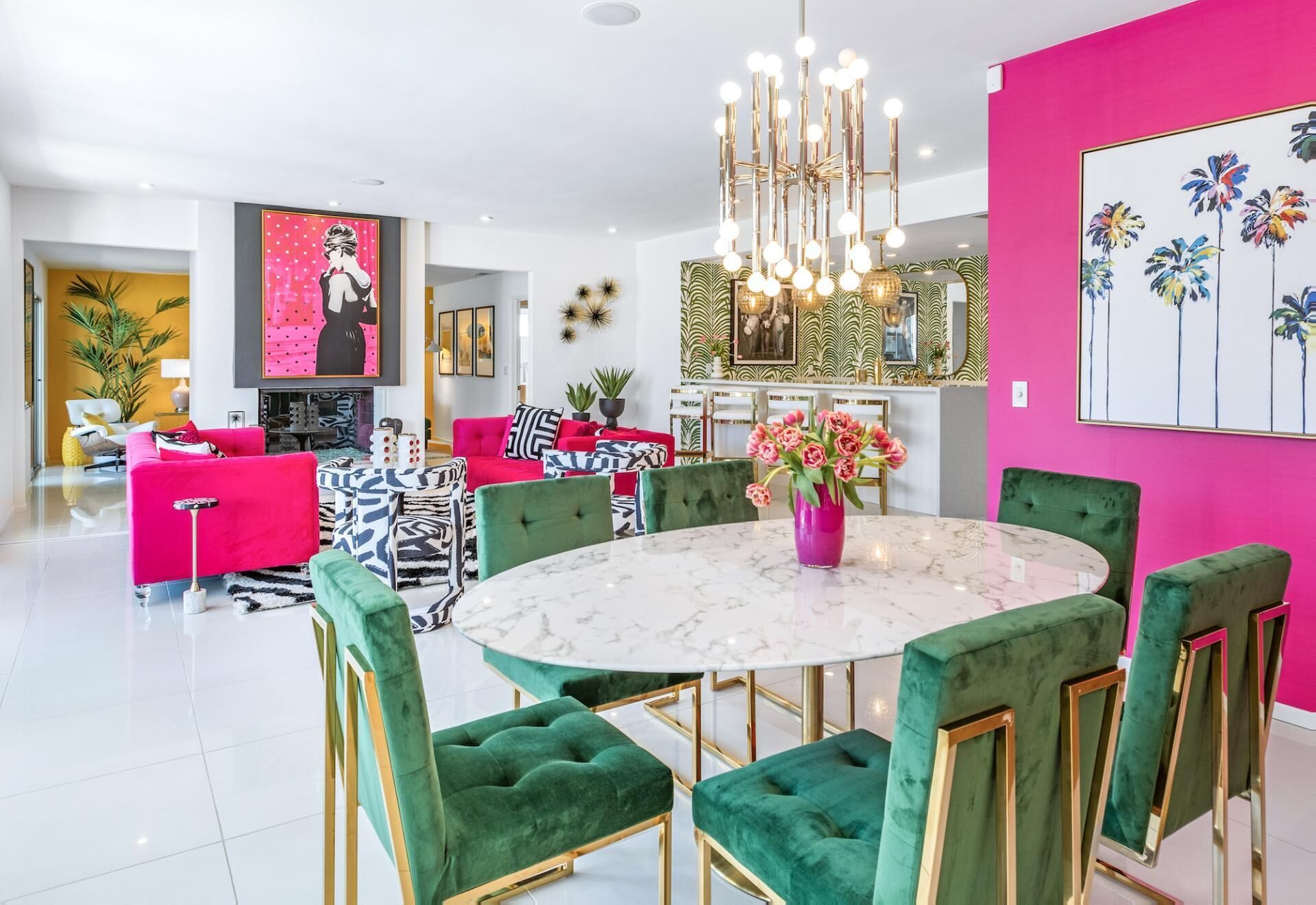 A modern living room with a round marble table, green upholstered chairs, and a vibrant pink wall.