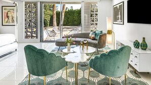 Una sala de estar moderna con un sofá gris, dos sillones de terciopelo verde, una mesa de centro y un televisor montado en la pared.