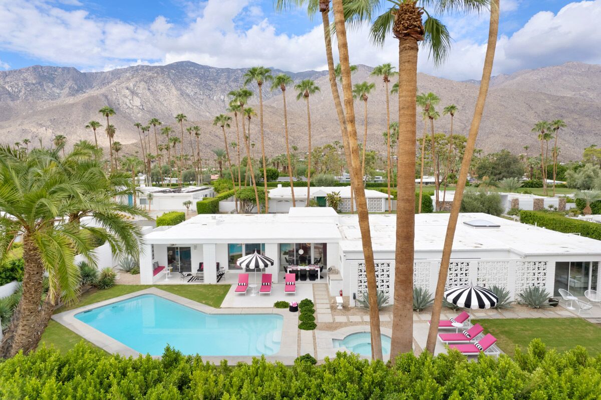 A modern resort with a pool, sun loungers, and palm trees.