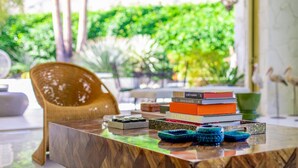 Une table en bois sur laquelle est posée une pile de livres, une paire de bols bleus et une chaise en osier, dans une pièce lumineuse donnant sur un paysage verdoyant.