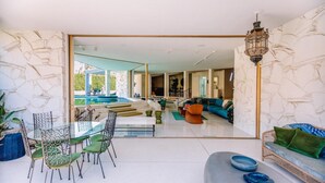 Un salon moderne avec une table à manger en verre, des chaises vertes, un canapé bleu et un mur en pierre.