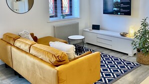 Un salon moderne avec un canapé, un miroir rond, un téléviseur et une lampe décorative suspendue.
