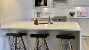 Une cuisine moderne avec des meubles blancs, un îlot central doté de tabourets, un four à micro-ondes et une machine à café.