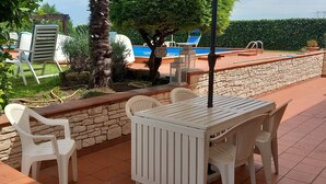 A patio area with a table and chairs, a stone wall, and a pool in the background.