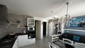 A modern kitchen with a dining area, featuring a stove, microwave, oven, and a glass dining table with chairs.