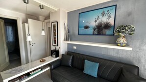 A modern living room with a black leather sofa, a white coffee table, and a painting of a landscape.