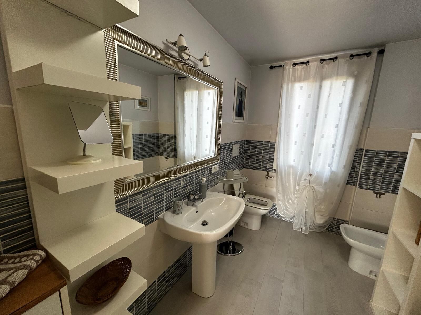 Une salle de bain moderne avec un grand miroir, un lavabo sur colonne, des toilettes et un espace douche.