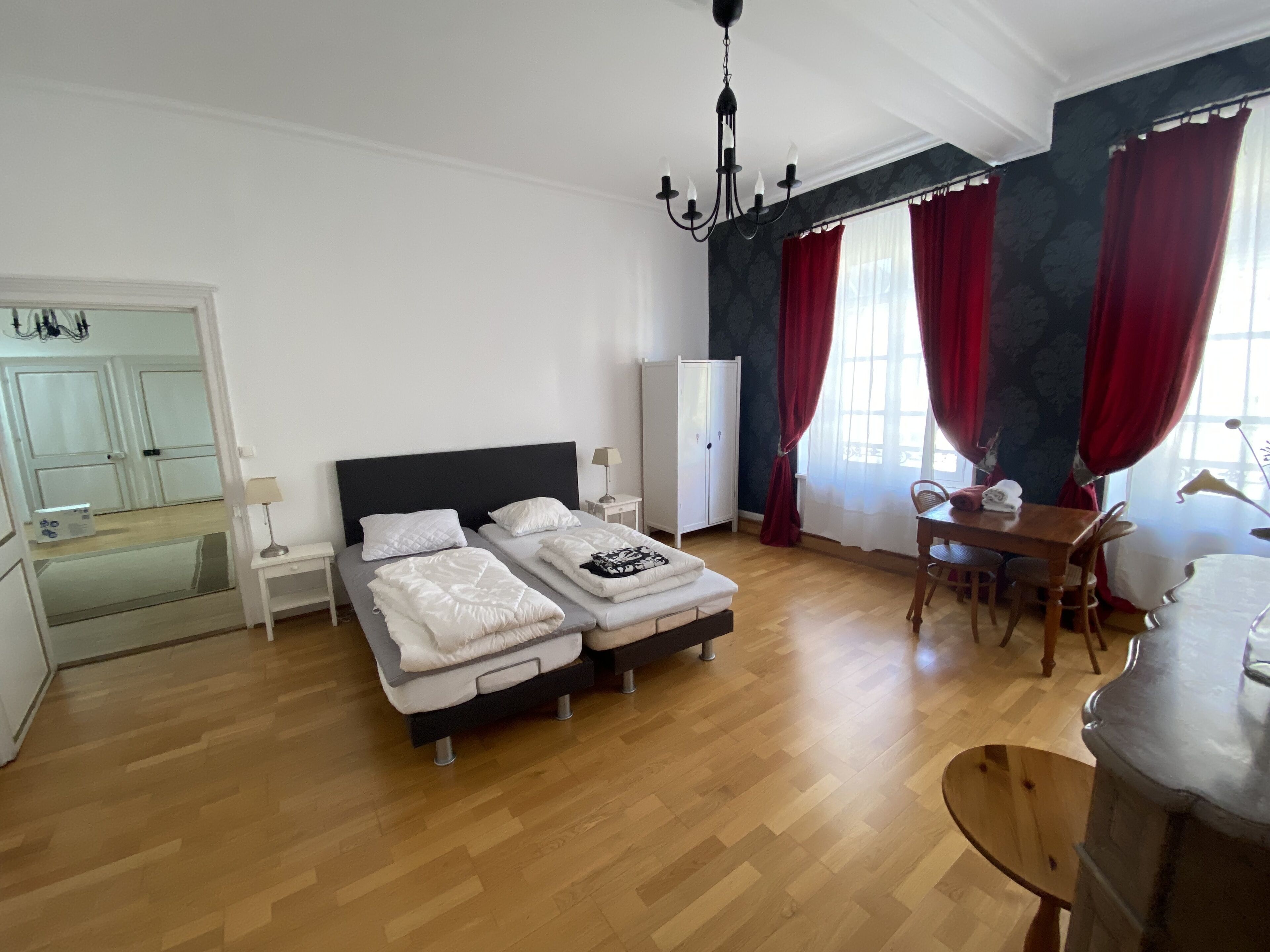 A bedroom with a double bed, a wardrobe, a desk with a chair, and a chandelier.