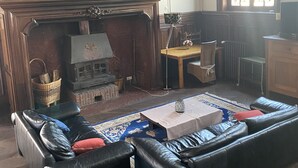 Olohuone, jossa on takka, nahkasohvat, sohvapöytä ja kattokruunu.