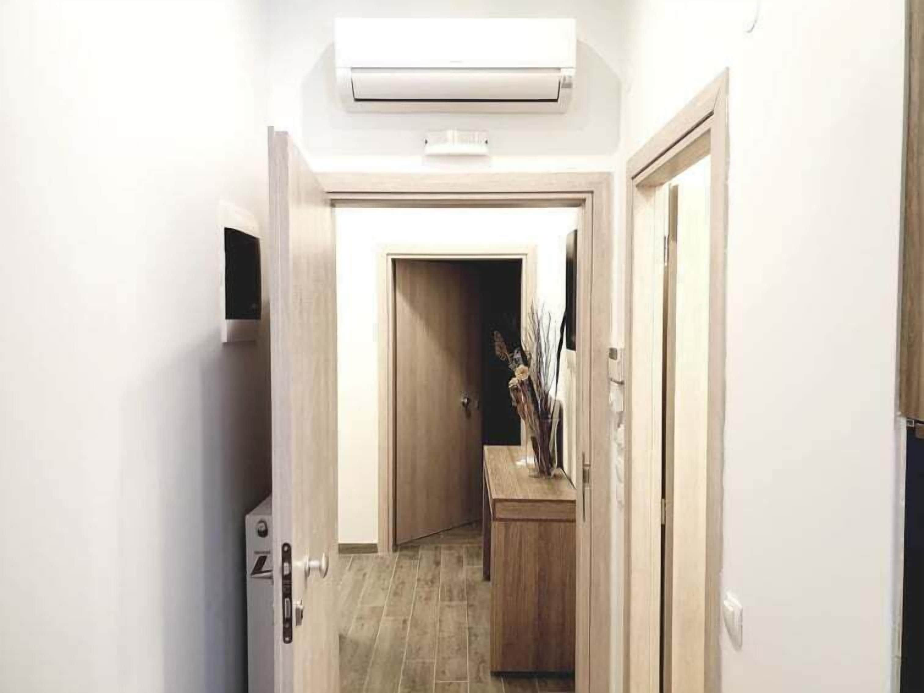A narrow hallway with a wooden door at the end, a small table with decorative items, and an air conditioning unit mounted on the wall.
