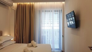 A hotel room with a bed, a TV mounted on the wall, and a window with curtains. - Eantos Studios and Suites (Thermaikos)