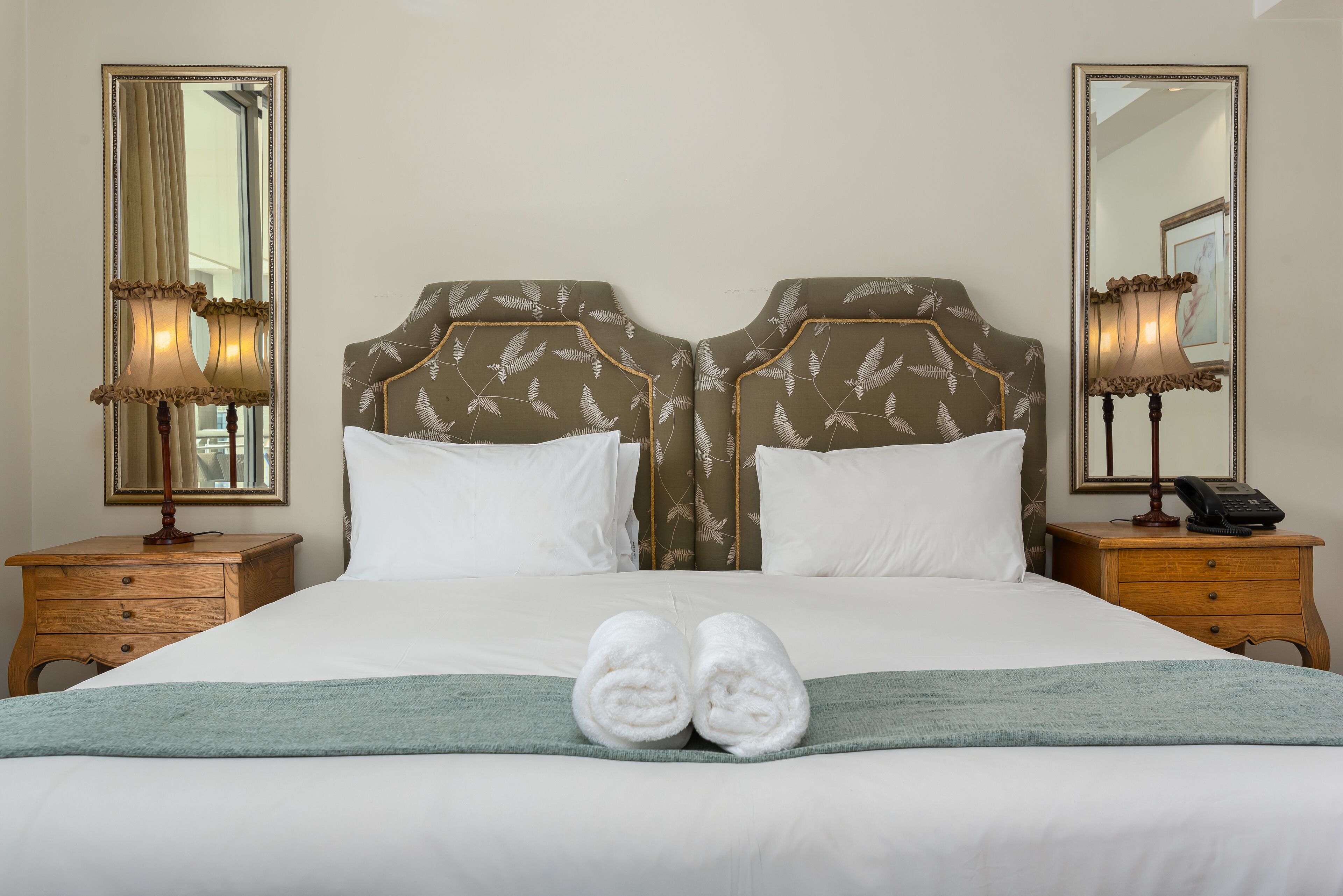 A neatly made bed with white linens, two bedside tables with lamps, and a large mirror on the wall.