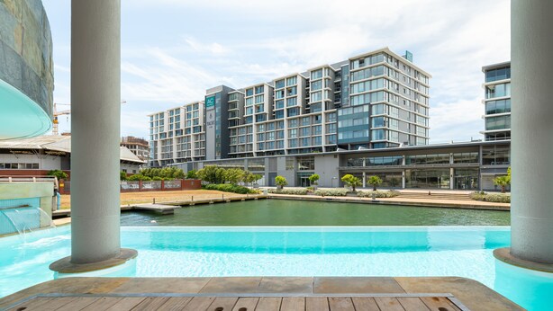 A modern hotel with a pool, a water feature, and a view of the surrounding area. - Canal Quays 607 (Cape Town)