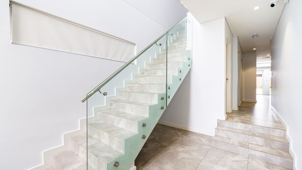 Eine moderne Treppe mit Glastrennstäben und beige marmornen Stufen.