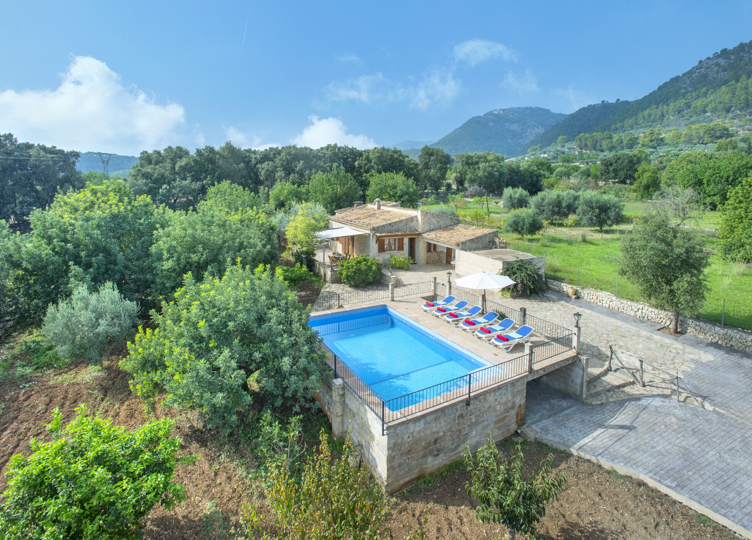 A pool with lounge chairs, a stone building, and surrounding greenery.