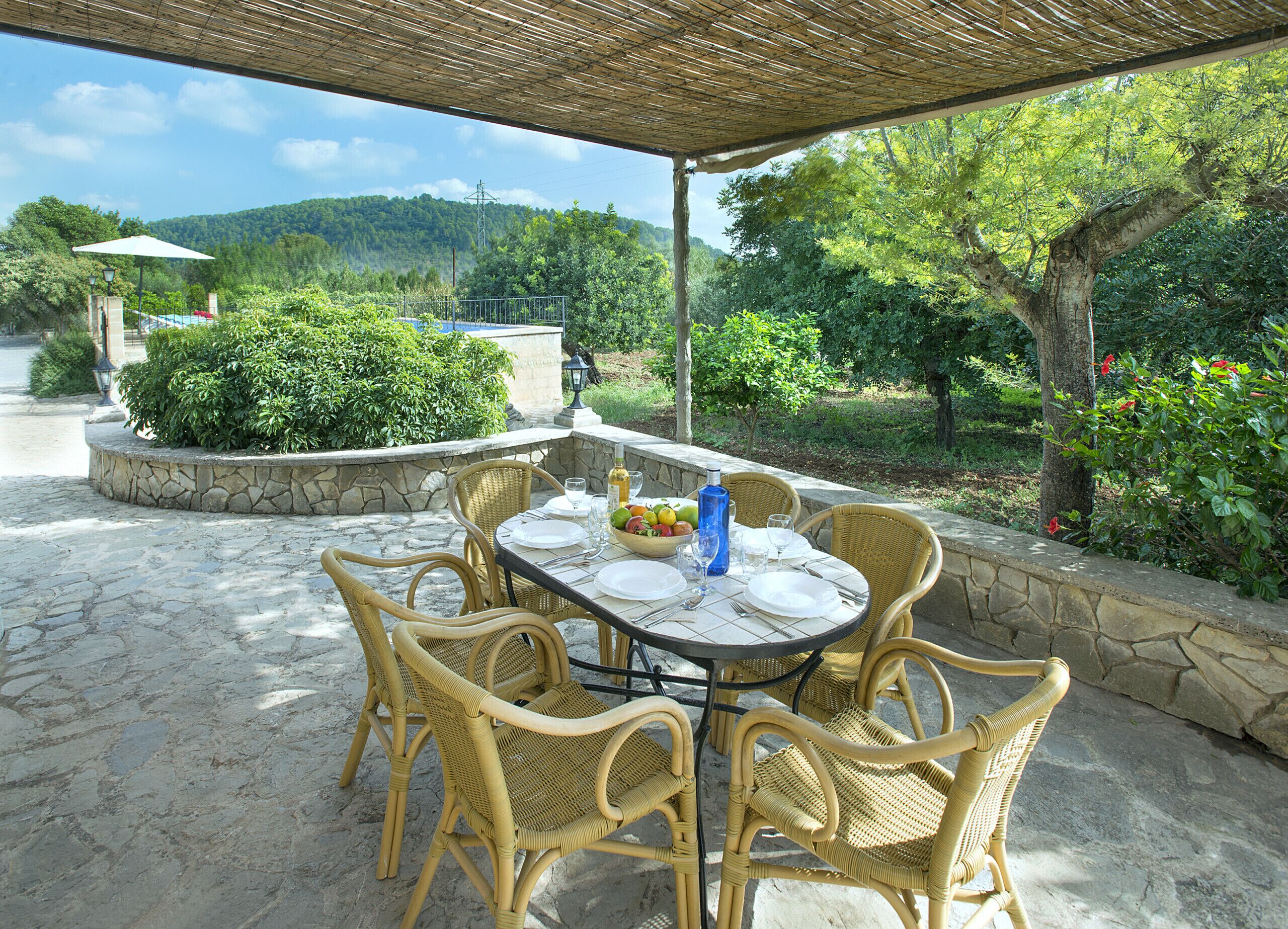 Un espace extérieur aménagé pour les repas, avec un sol en pierre, des chaises en osier et une table dressée pour quatre personnes.