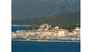Una cittadina costiera con un porto turistico, edifici storici e montagne sullo sfondo.