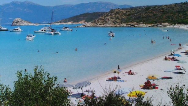 Una spiaggia con barche, persone che nuotano e ombrelloni.