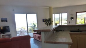 Una cucina moderna con isola centrale, un'area pranzo con divano rosa e una TV nella zona living.