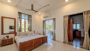 Une chambre spacieuse avec un grand lit, un ventilateur de plafond et un balcon avec vue.