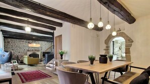 Amplia sala de estar con chimenea de piedra, vigas de madera y una mesa de comedor con sillas.