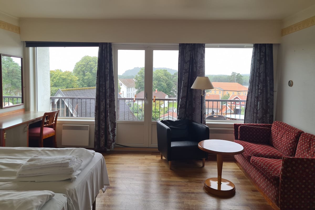 A hotel room with a bed, a desk, a chair, a sofa, a small round table, and a window with curtains.