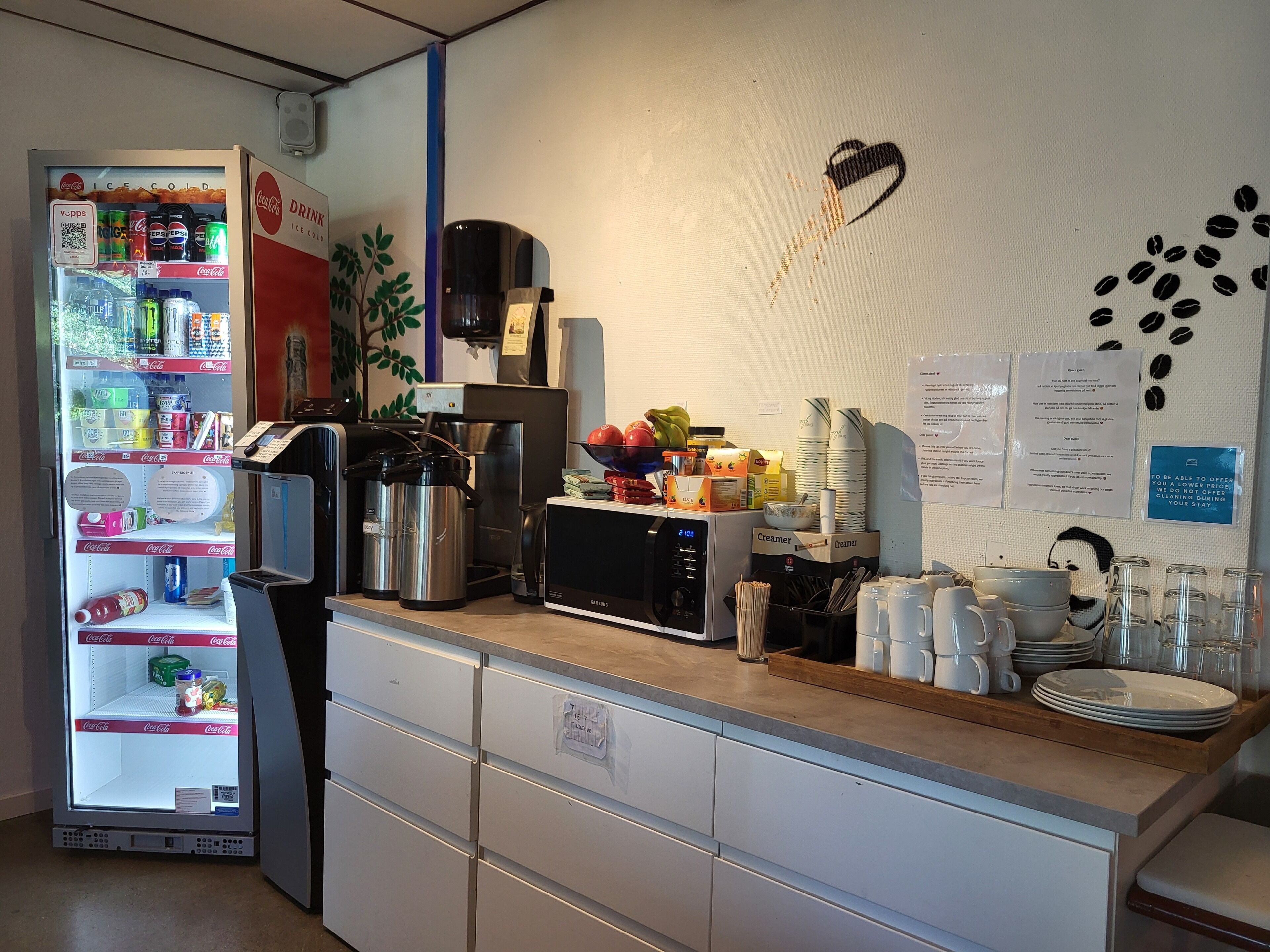 A kitchen area with a refrigerator stocked with beverages, a coffee machine, and various kitchen utensils.