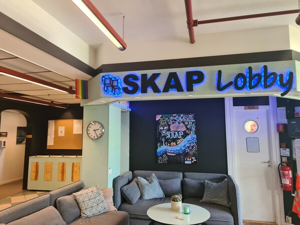 A lobby area with a sofa, a small table, a wall clock, and a sign that reads "SKAP Lobby".