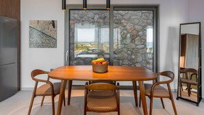A modern dining area with a wooden table and chairs, a fruit basket, and a view through a glass door to an outdoor area. - Modern Villa Omega with Private Pool (LEFKADA)