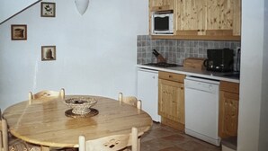 Ett kök med träskåp, en mikrovågsugn, en spis och en diskmaskin. Där finns ett runt träbord med stolar.