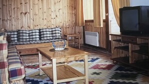Ett mysigt vardagsrum med en väggpanel av trä, en rutig soffa, ett litet bord, en tv och en mönstrad matta.