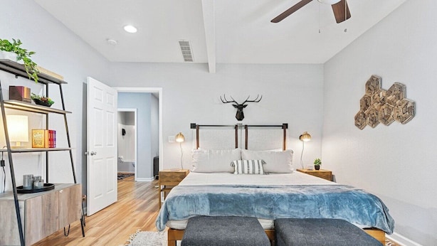 A bedroom with a bed, bedside tables, a ceiling fan, a wall-mounted deer head decoration, and a wooden floor.