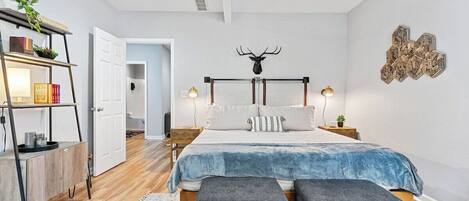 A bedroom with a bed, bedside tables, a ceiling fan, a wall-mounted deer head decoration, and a wooden floor.