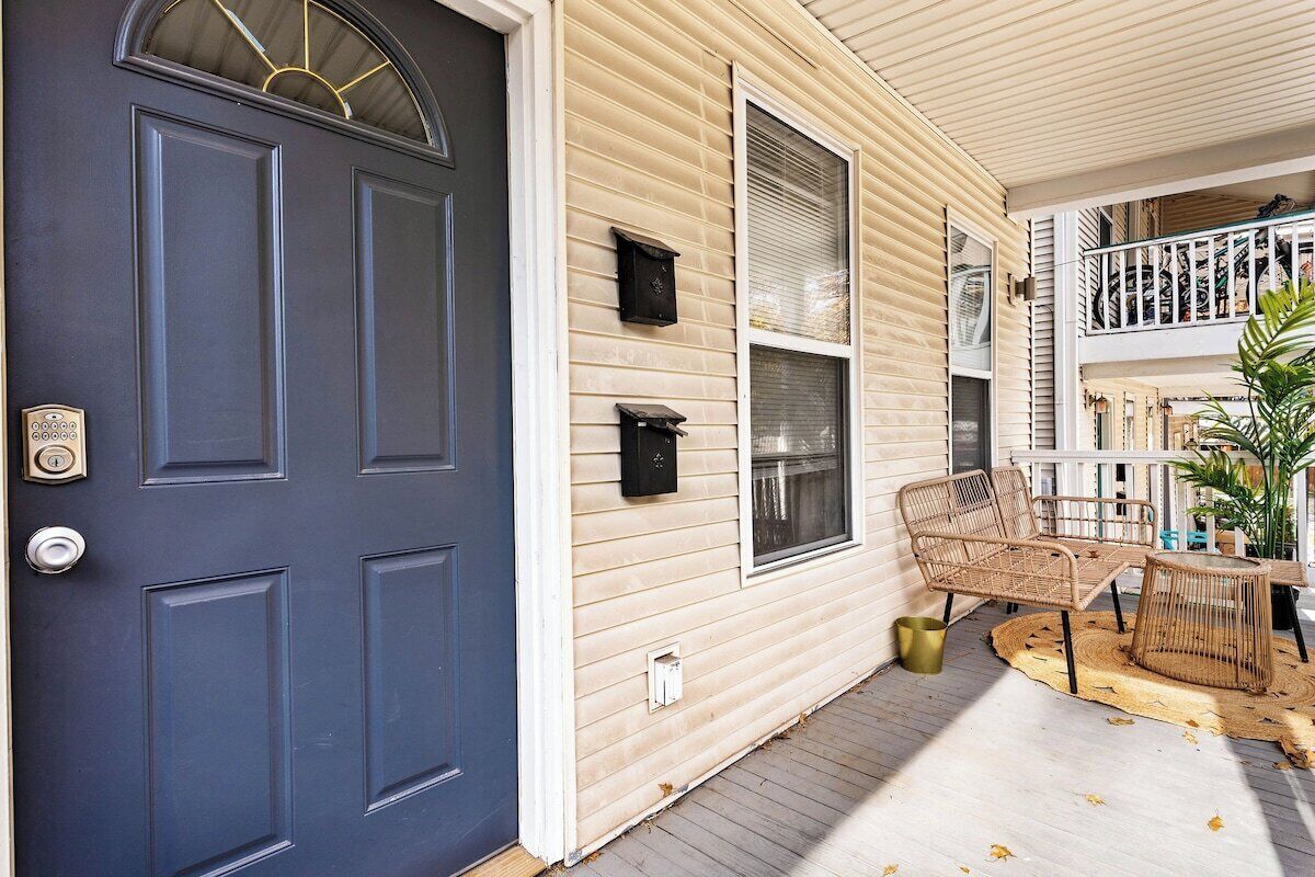 A two-story house with a dark blue front door, beige siding, and a covered porch with wicker furniture.