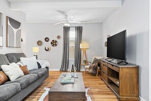 Una sala de estar con un sofá gris, una mesa de centro, un televisor y un ventilador de techo.