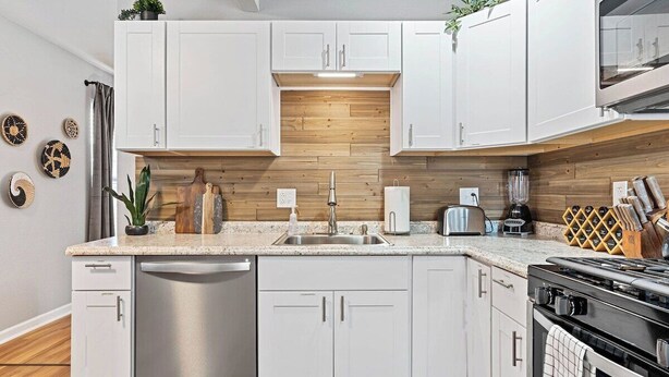 A modern kitchen with white cabinets, stainless steel appliances, and a wooden backsplash. - Columbus Park Upper Apt Minutes from Downtown KC (Kansas City)